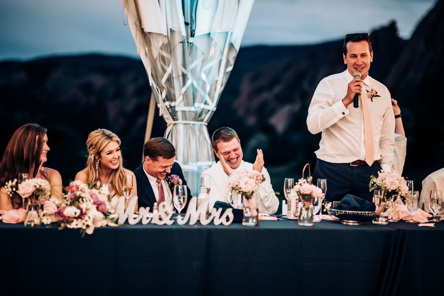 Wedding reception speech with audience reactions at outdoor venue.