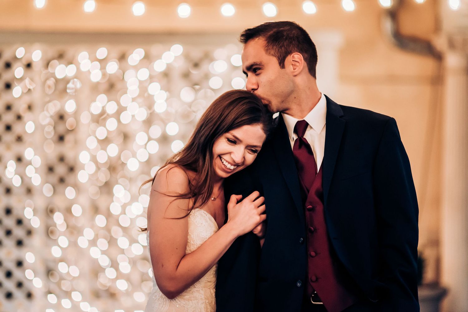 A couple embraces in front of a sparkling light wall backdrop at their wedding celebration.