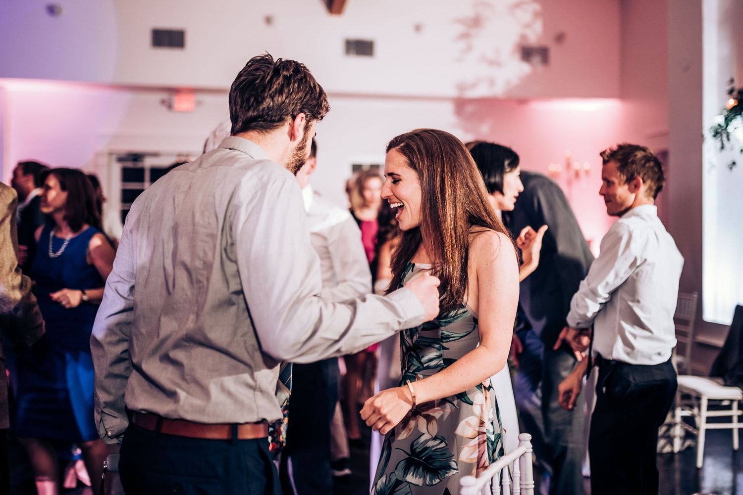 Couples dance and laugh together during a lively wedding reception with pink ambient lighting.