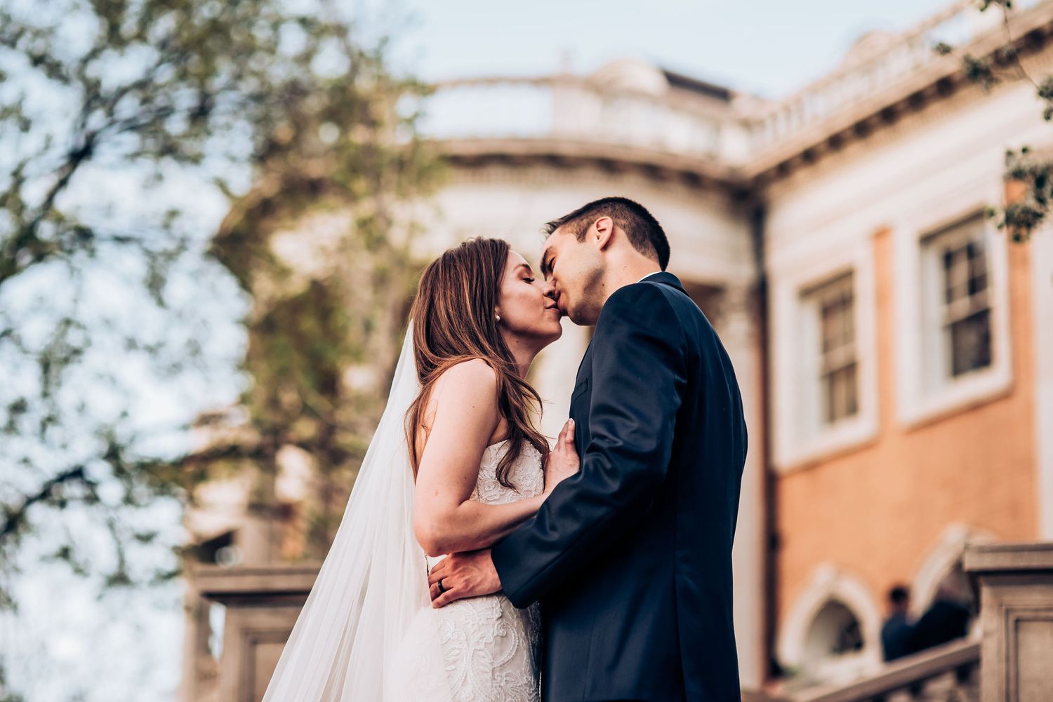 Intimate wedding kiss captured against warm terracotta walls of historic venue.