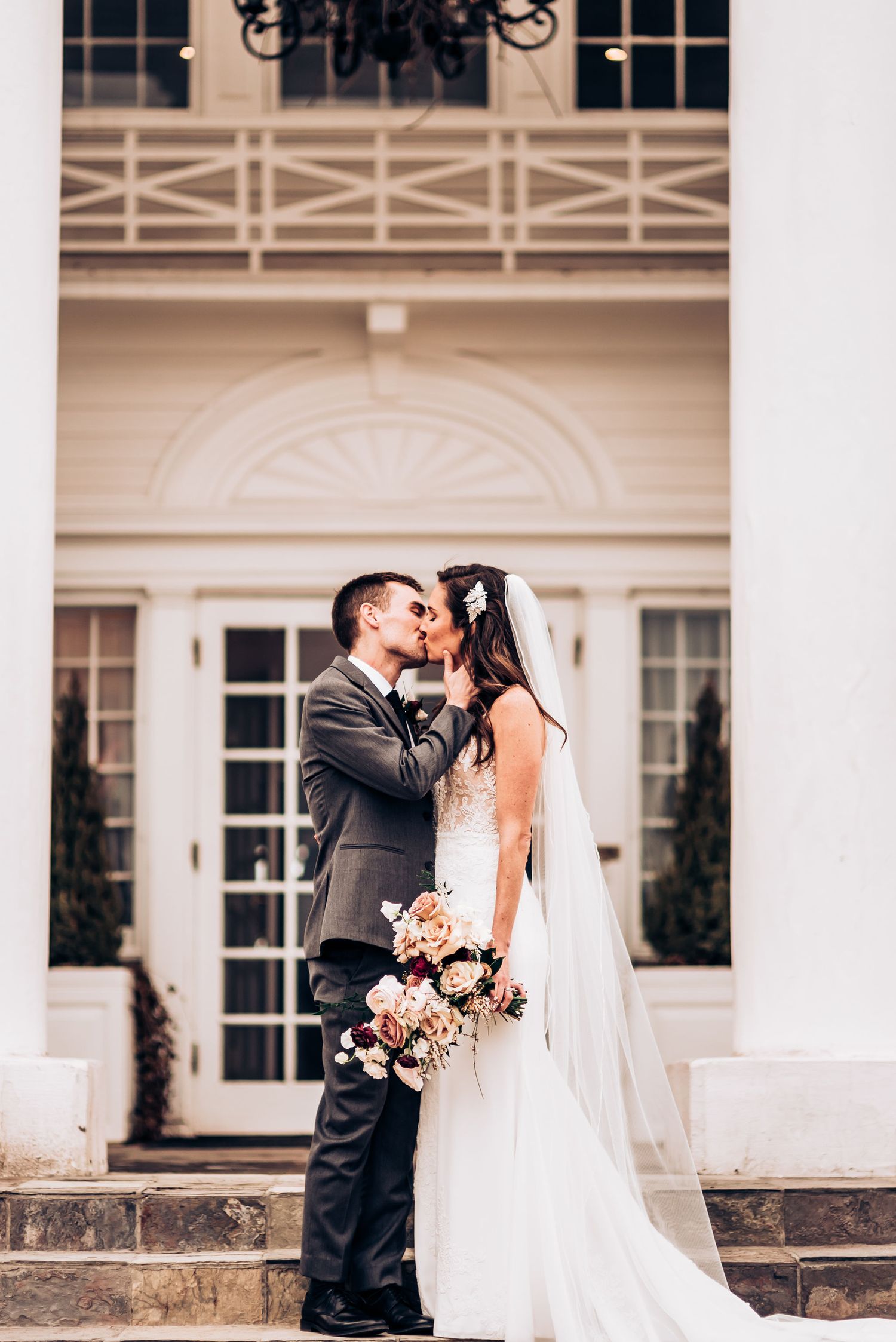 Romantic wedding portrait on mansion steps with white columns and elegant architecture.