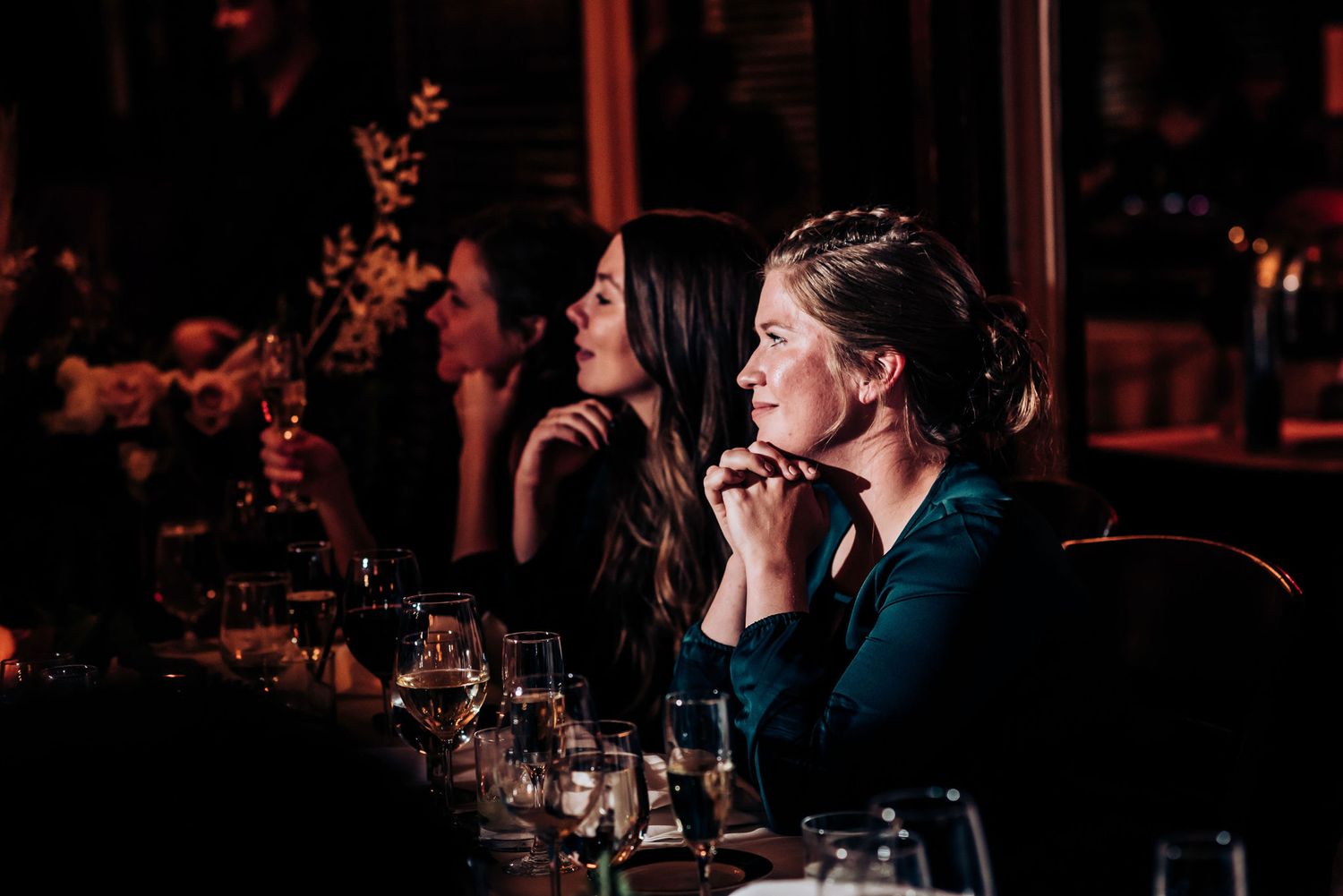 A candlelit dinner reception with guests seated at tables in dark atmospheric lighting.