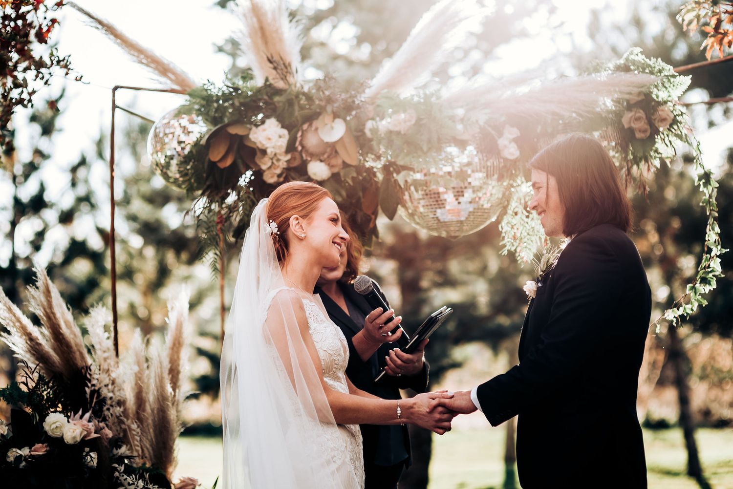 Intimate outdoor wedding vow exchange beneath decorative floral arch.