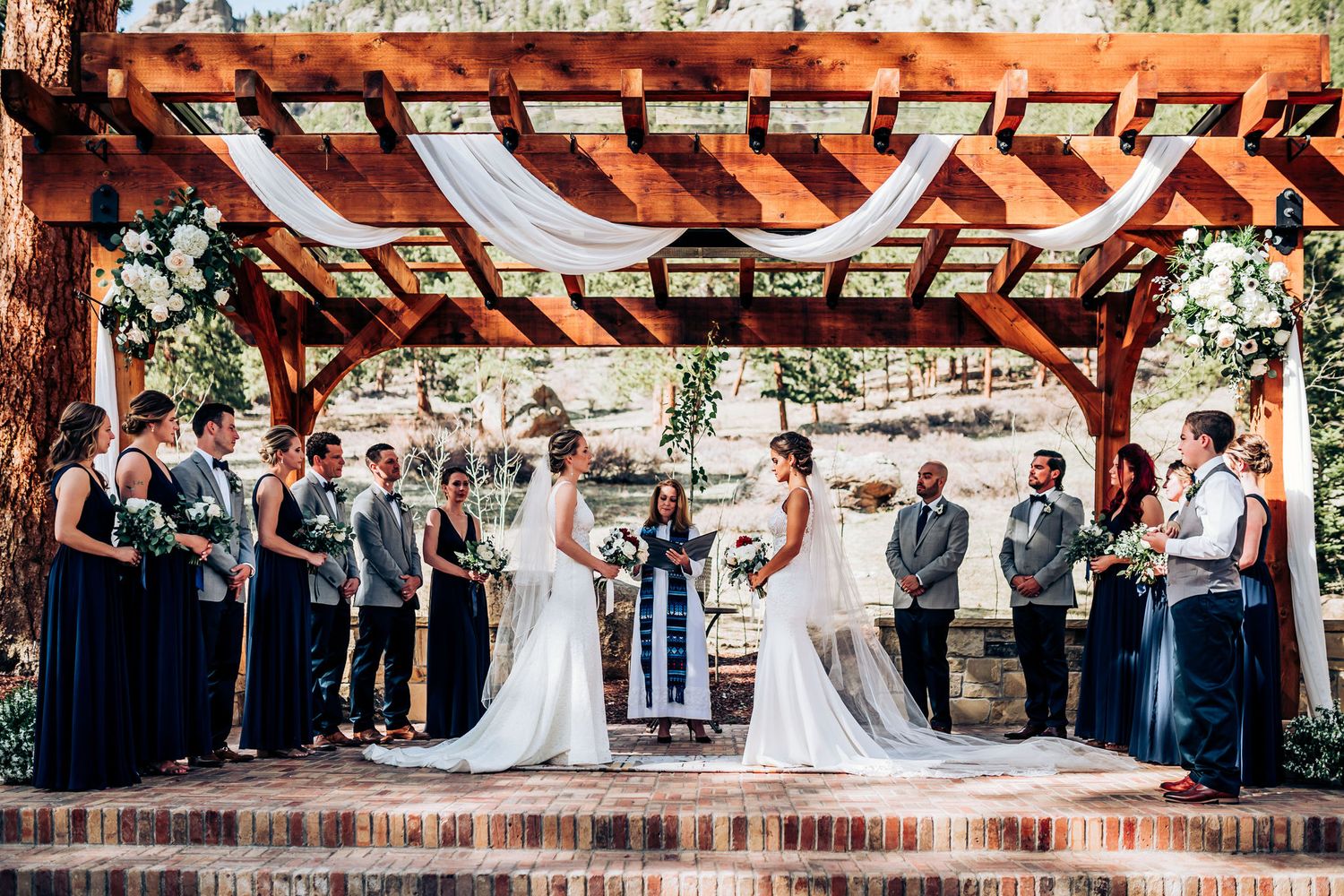 Wedding ceremony under a rustic wooden pergola with white draping and mountain views.