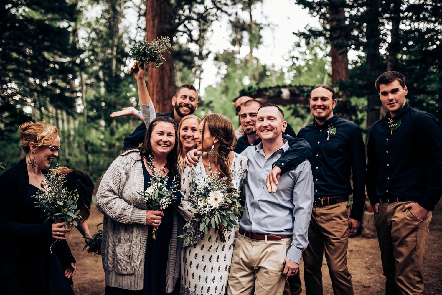 Group celebration photo with friends in formal attire outside in a pine forest.