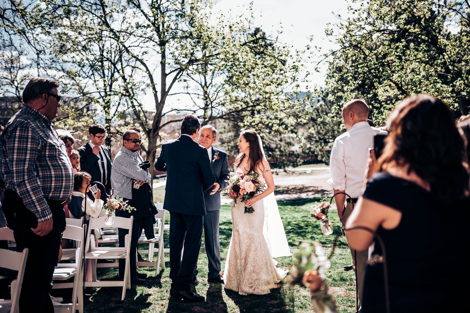 Outdoor wedding ceremony takes place surrounded by blooming spring trees and seated guests.