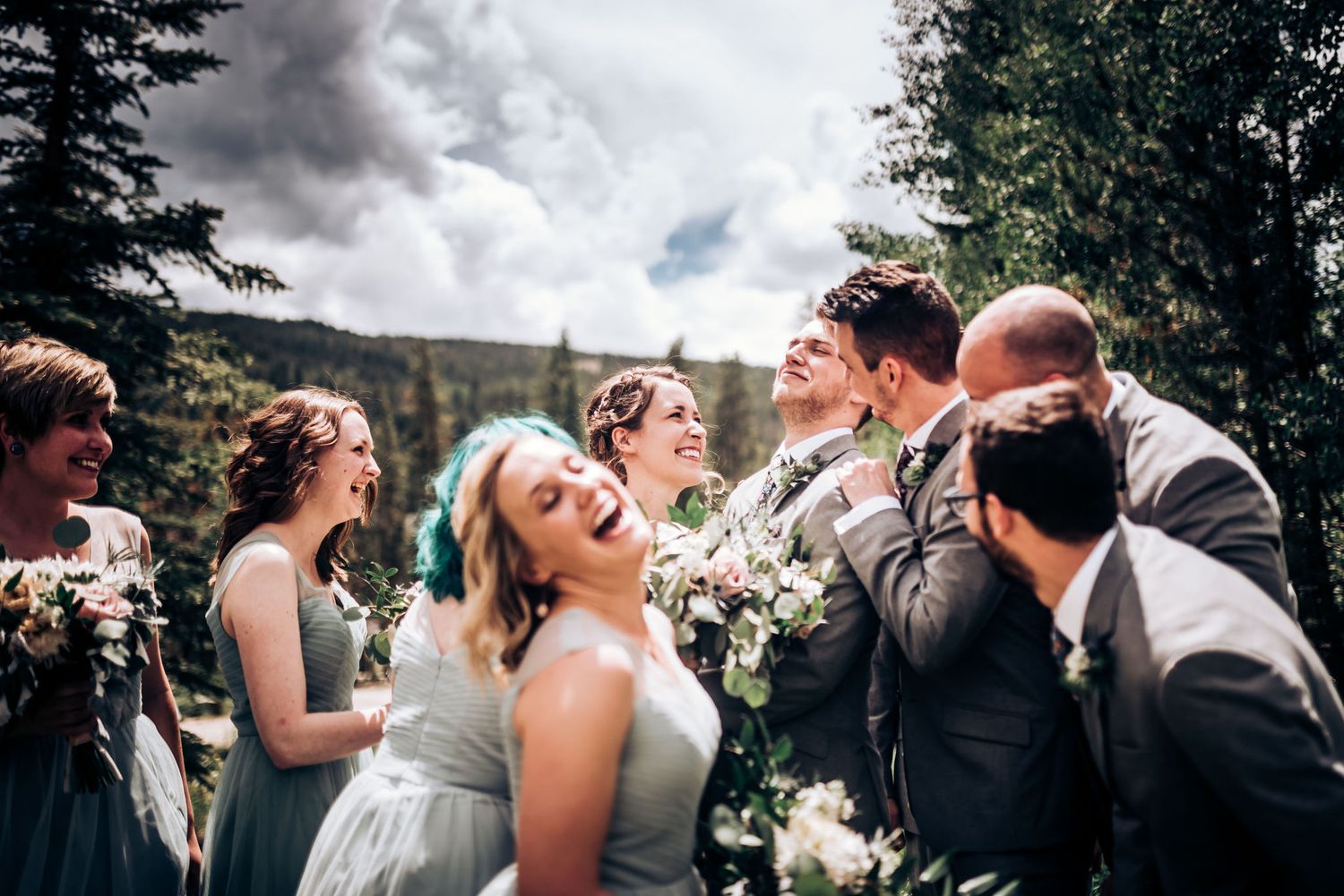 A candid moment of laughter shared between a wedding party in a mountain setting.