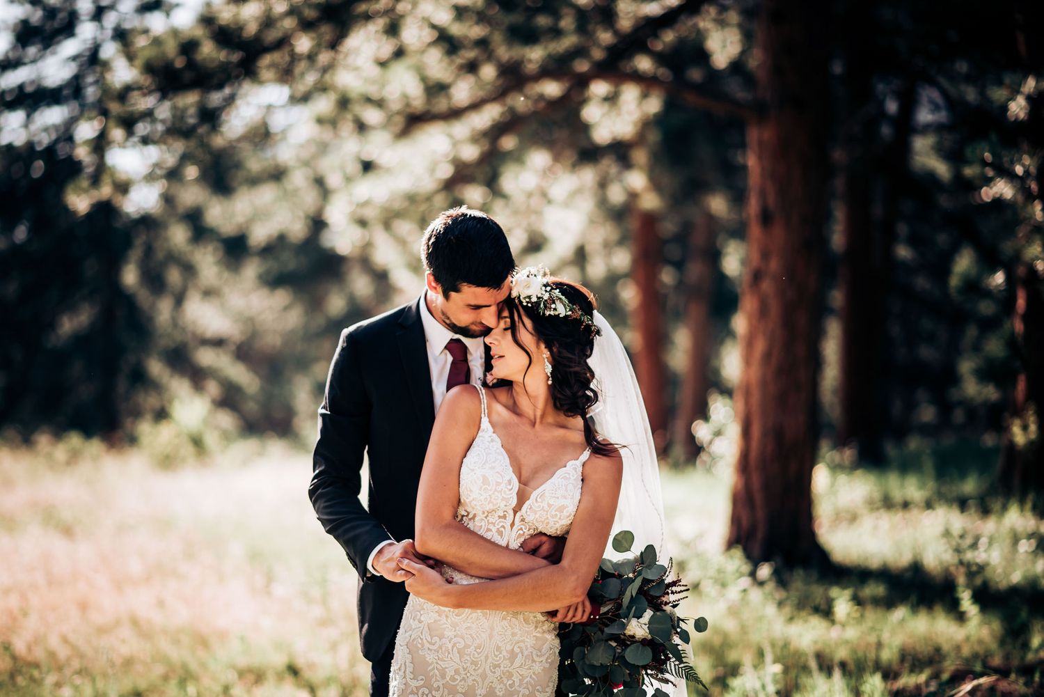 Romantic wedding moment captured in a sunlit forest clearing with mountain backdrop.