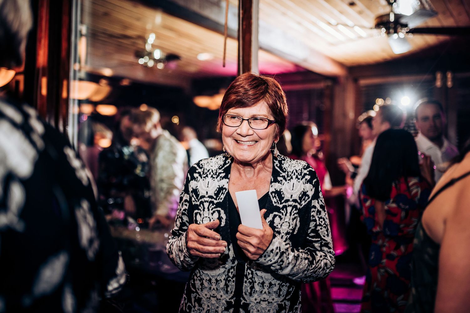 Person wearing a floral print jacket holds drinks on the dance floor at a celebration.