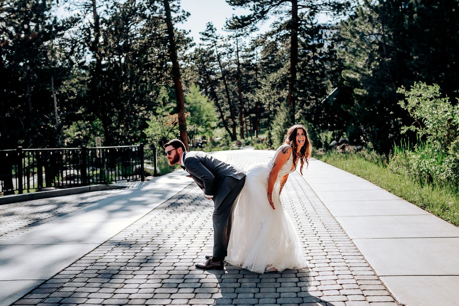 Playful wedding couple poses for fun photo on stone pathway with mountain scenery.