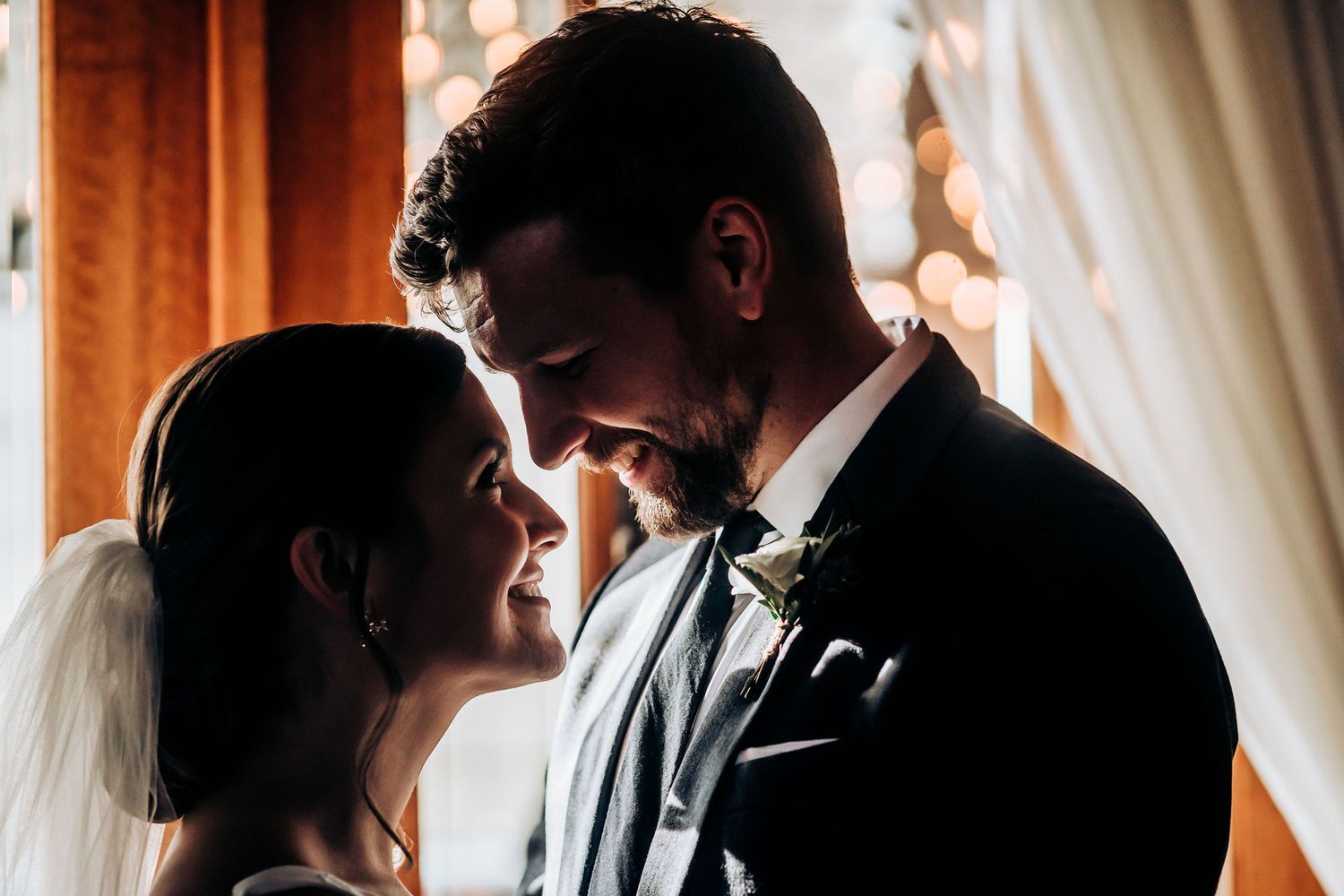 Silhouetted wedding couple sharing an intimate moment by window light.