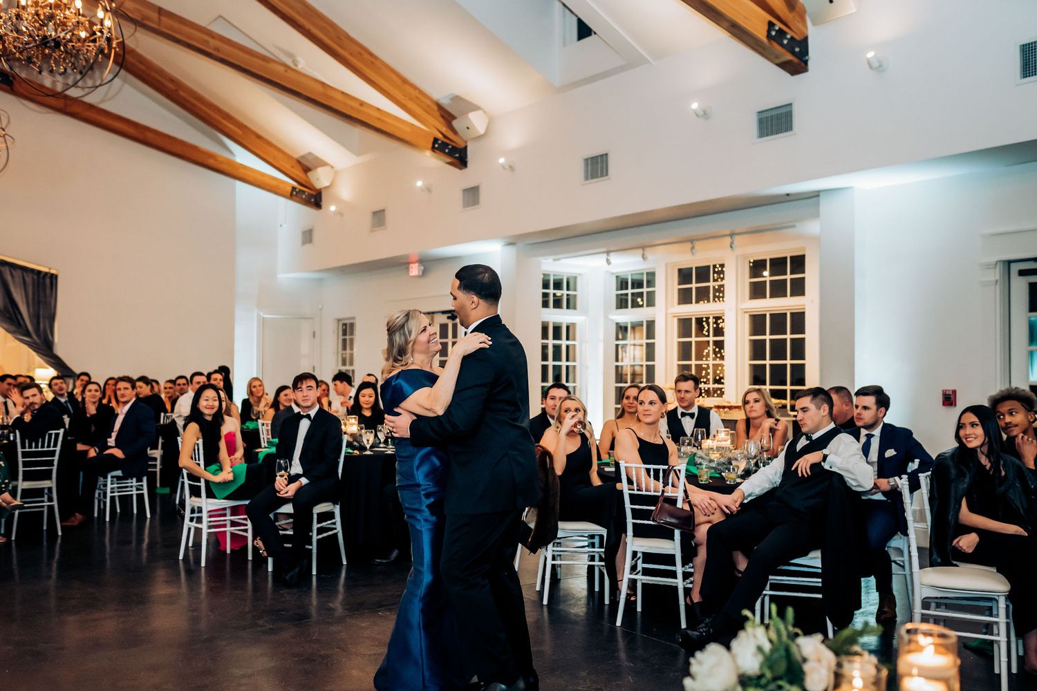 A romantic dance in a reception hall with exposed wooden beams and window panels.