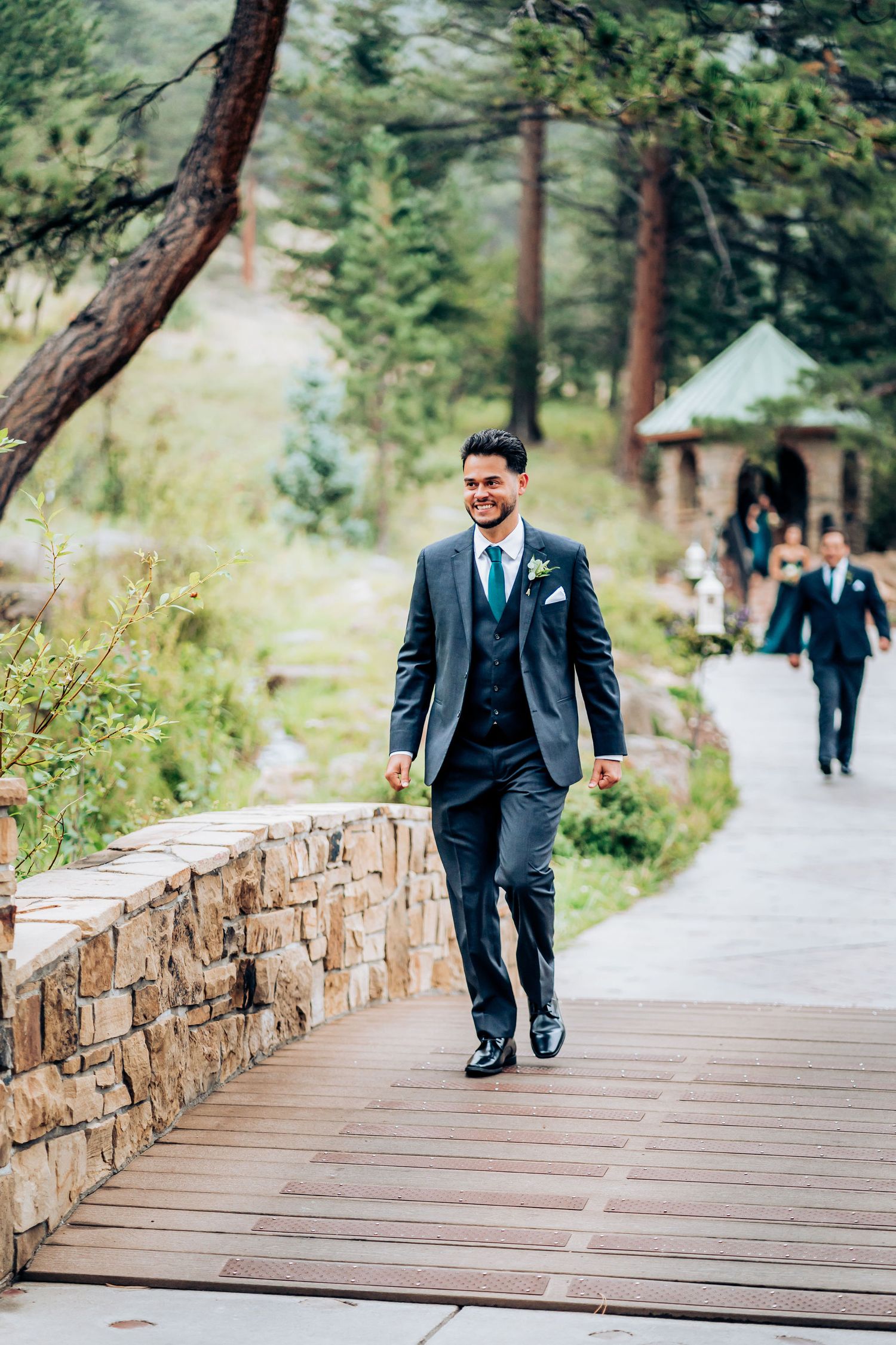 Person in three-piece suit walking along stone-lined pathway through mountain landscape.