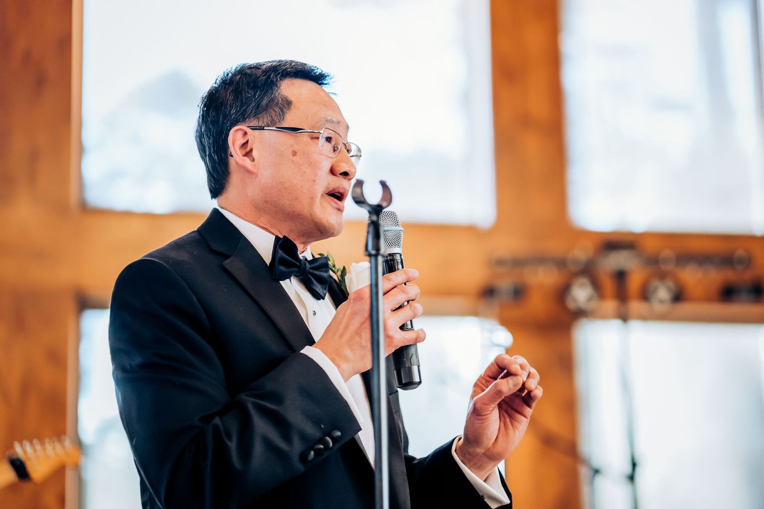 Speaker in formal attire delivers a speech at an elegant indoor venue with wooden accents.