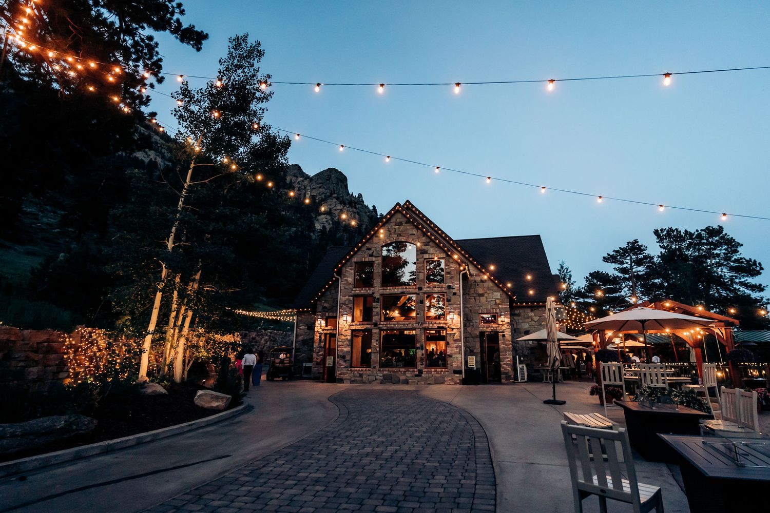 An outdoor wedding venue at dusk with string lights and rustic barn architecture.