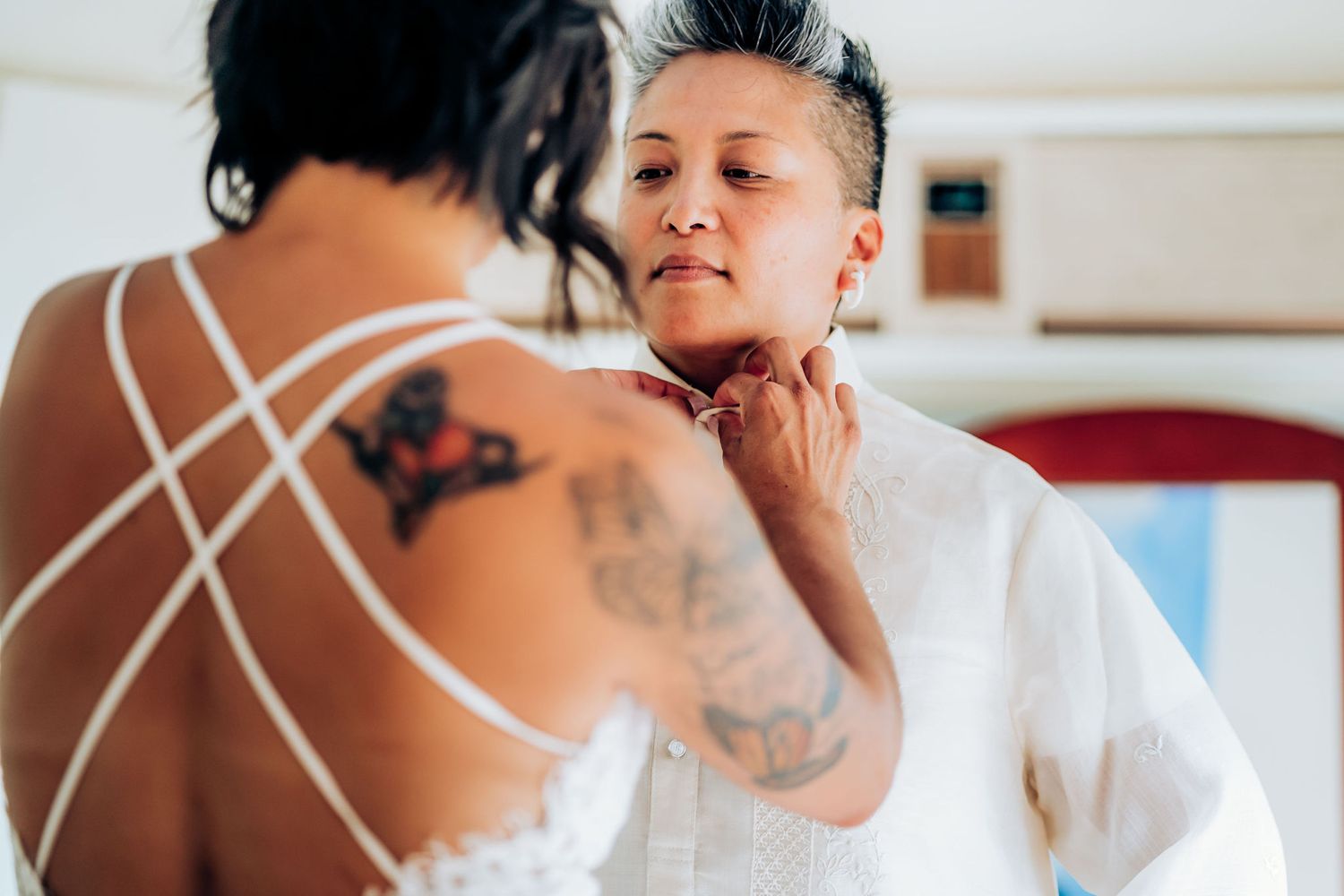 Close-up shot of someone applying makeup in a white outfit with strappy dress details and visible tattoos.