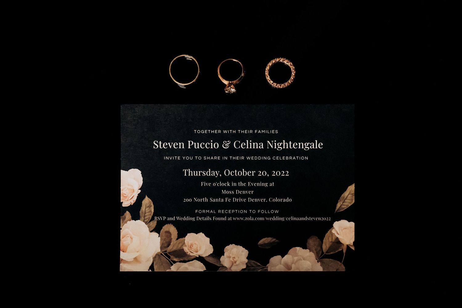 Wedding rings artistically photographed against a dark background with an invitation card.