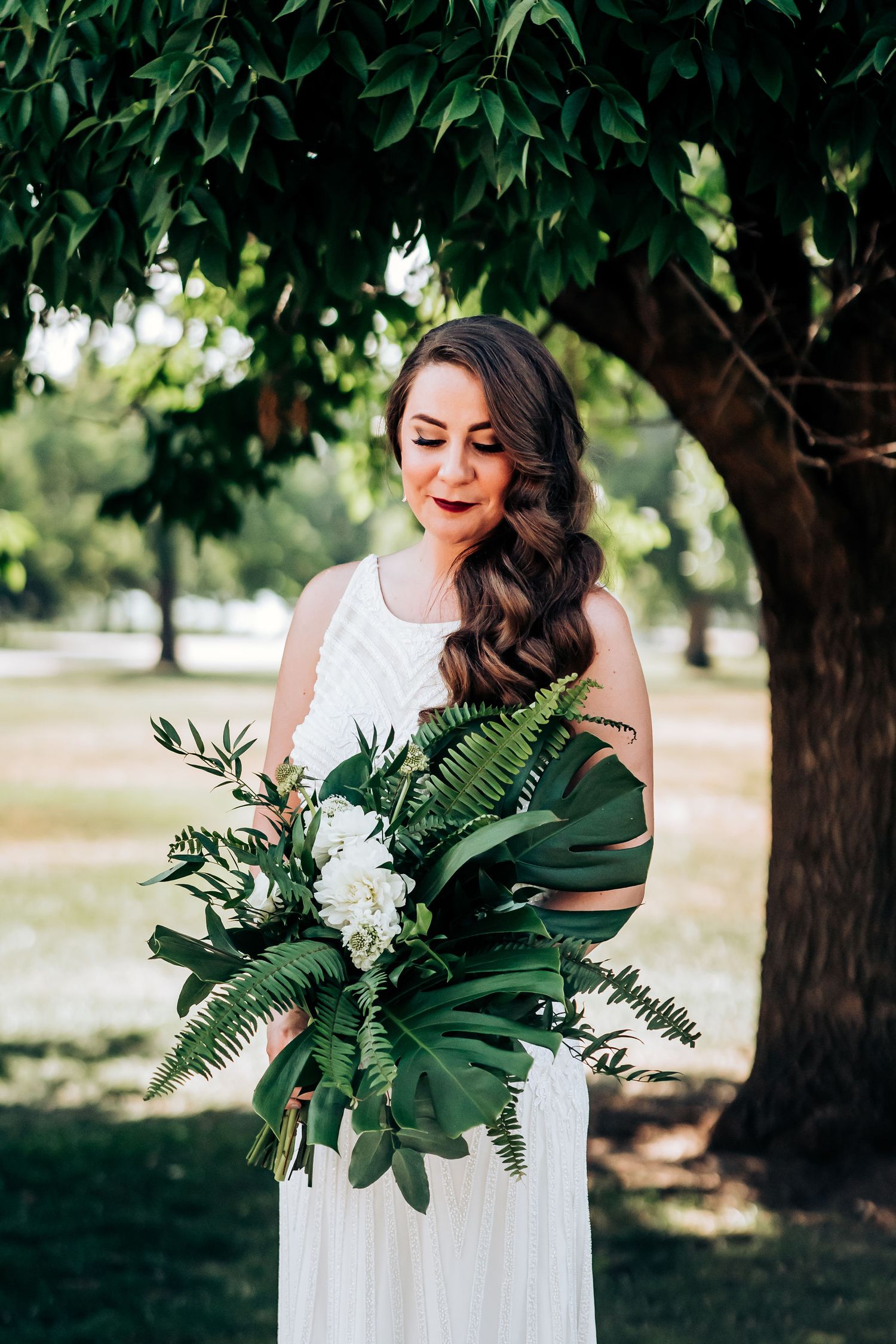 An elegant bridal portrait outdoors featuring a white gown and lush green tropical bouquet.