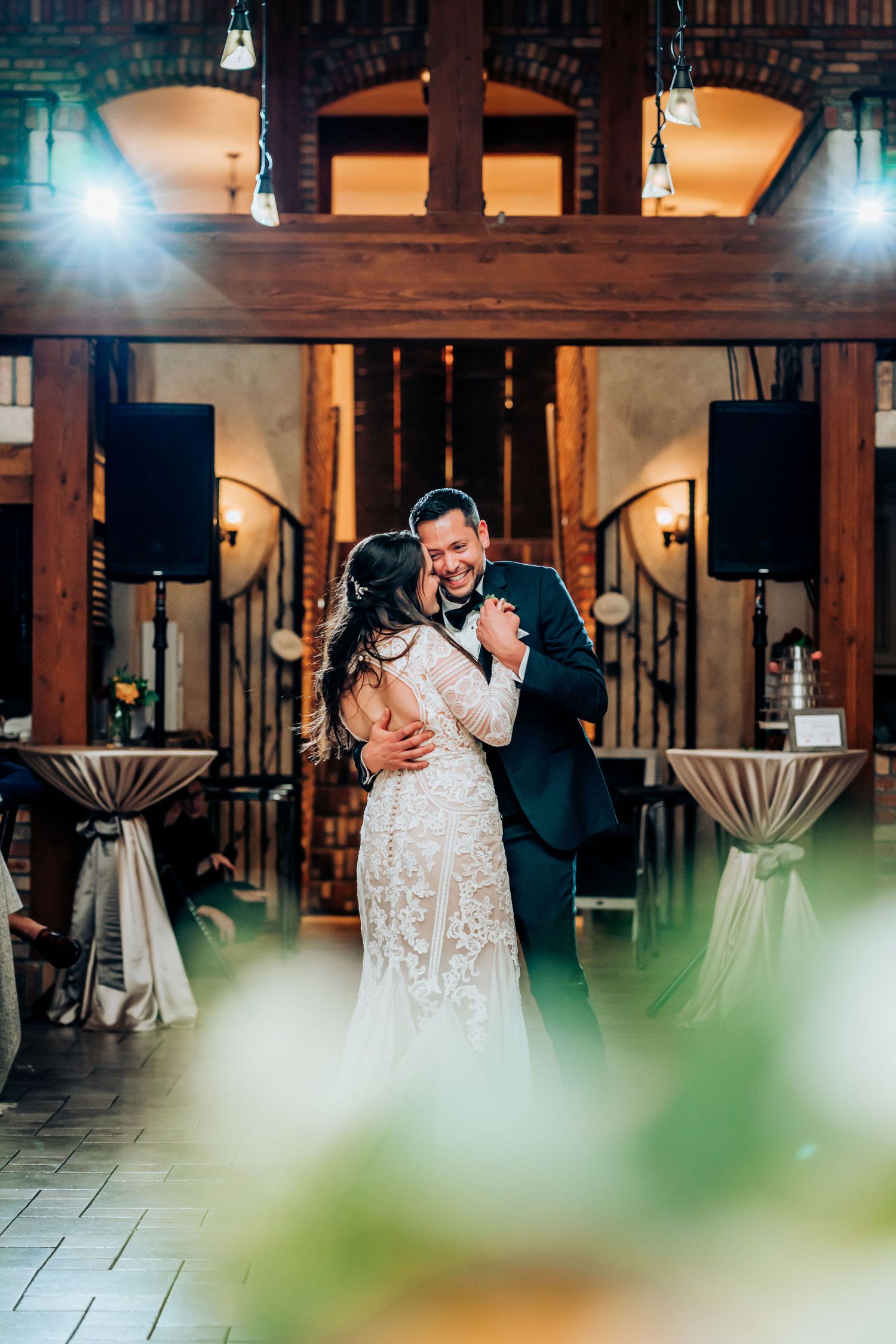 A romantic first dance moment in an elegantly lit venue with wooden beams and cocktail tables.