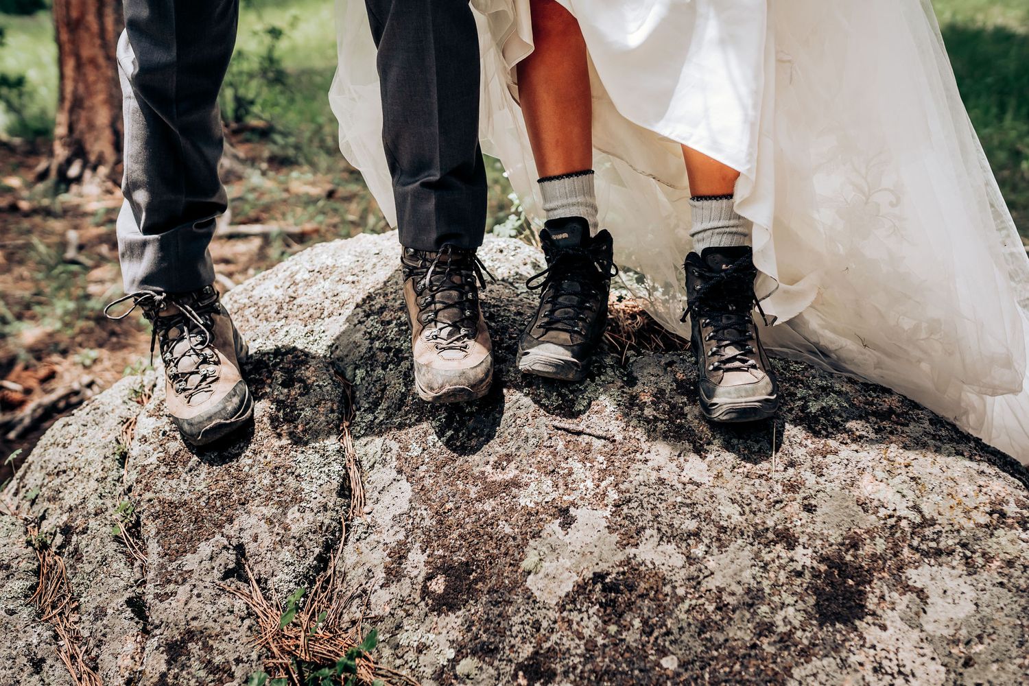 Close-up shot of bride and groom's hiking boots standing together on a rocky surface.