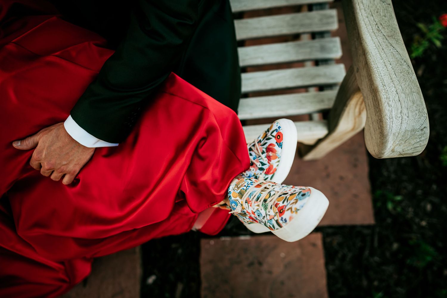 Close-up of floral patterned sneakers worn with a red formal dress.