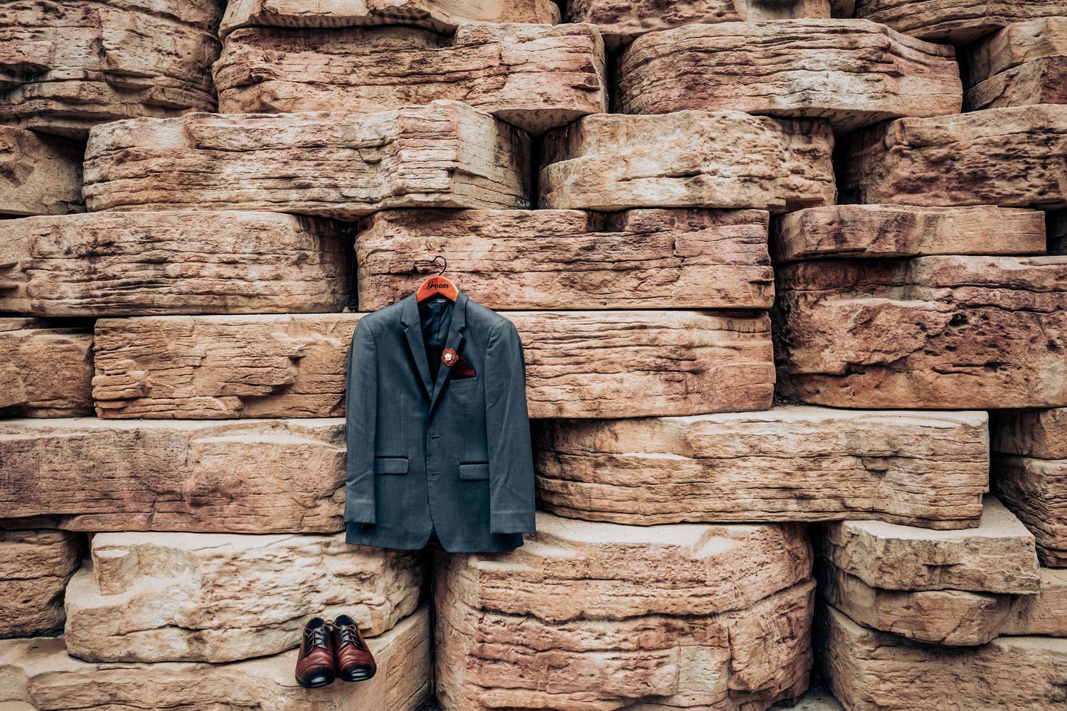 A blue suit jacket and dress shoes arranged on a textured rock wall.