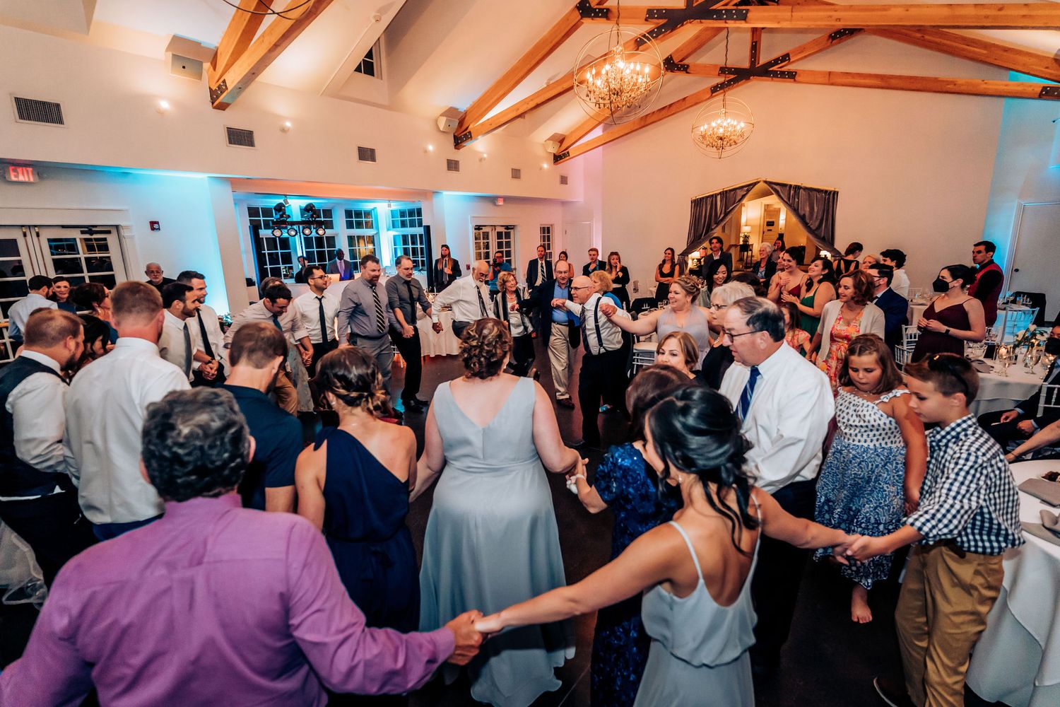Wedding guests dance together on crowded reception dance floor with blue mood lighting.