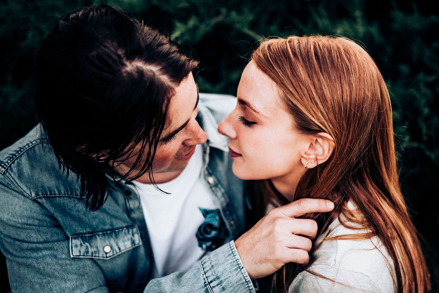 A tender moment between a couple in casual clothing against a dark background.