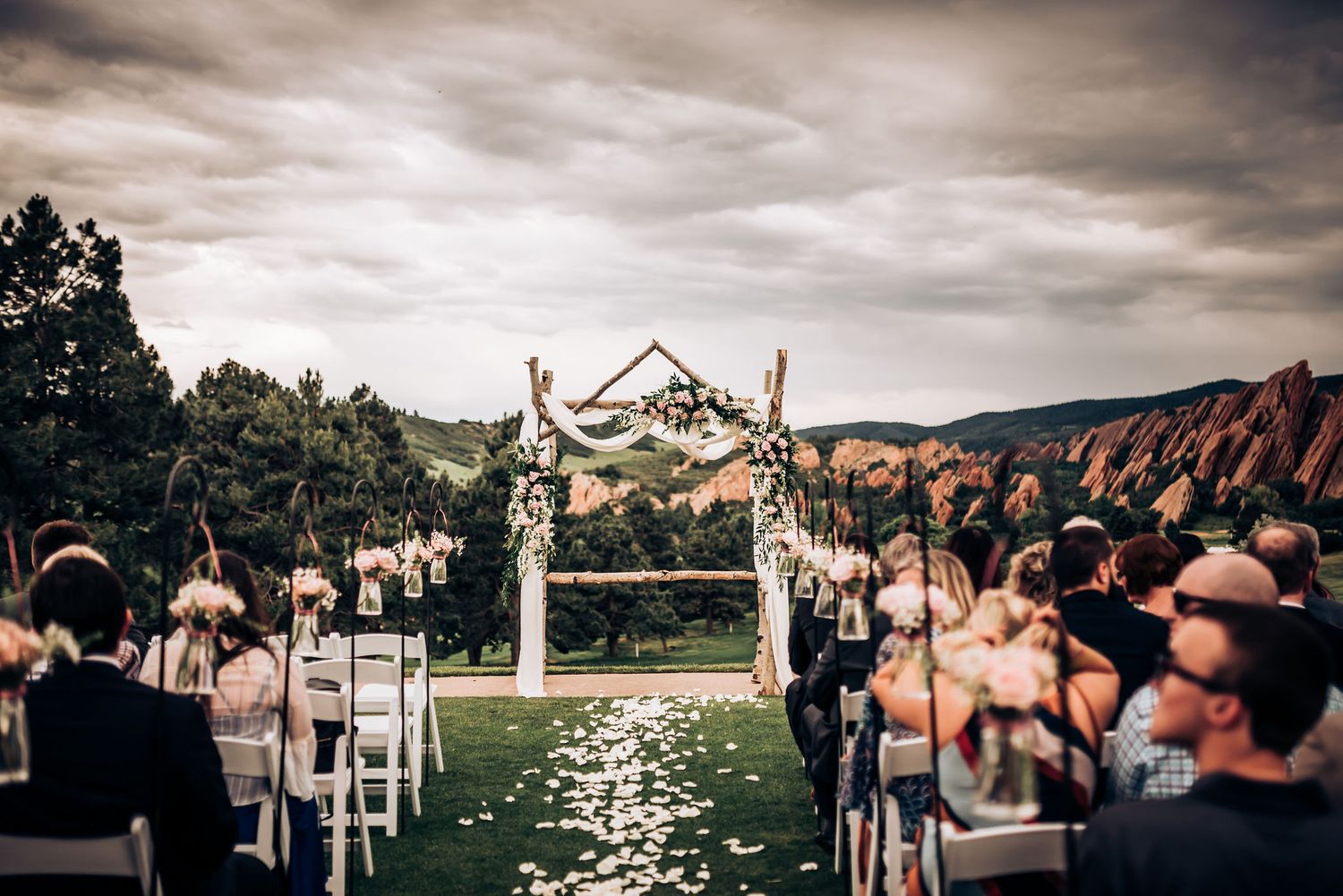 Outdoor wedding ceremony setup with flower-decorated arch and white petals lining the aisle.