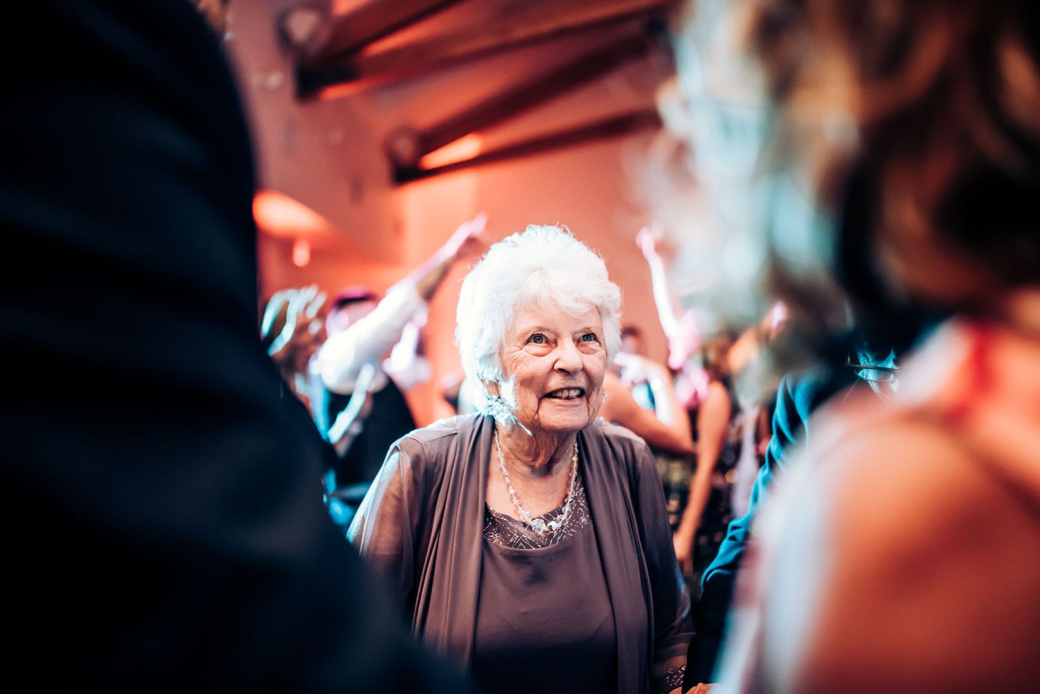An elegant elderly guest shares a joyful laugh on a festively lit dance floor.