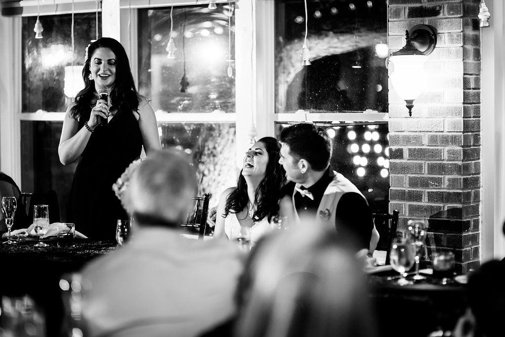 Black and white photo of reception speech with guests seated at decorated tables.