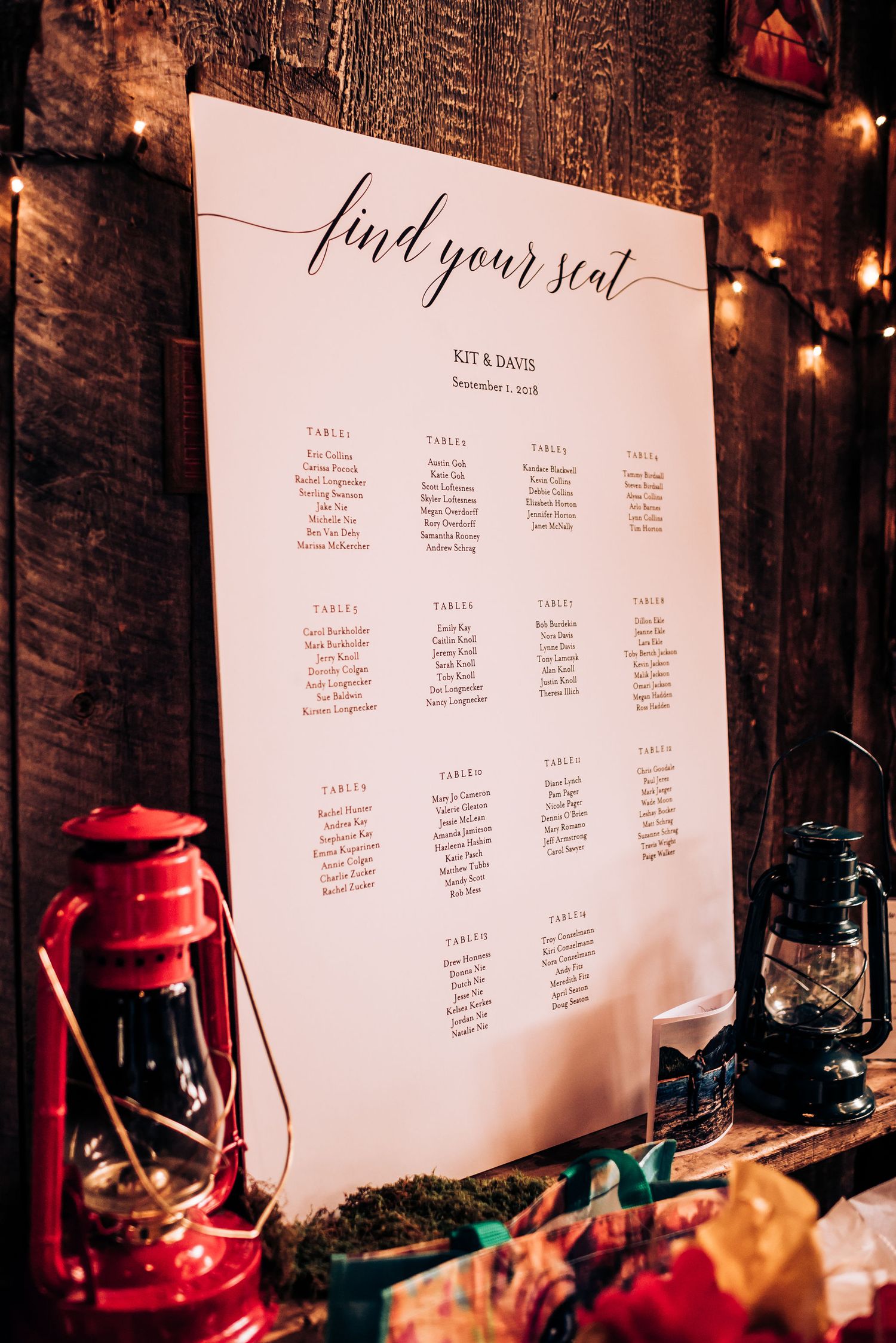 Wedding seating chart with lantern decor against wooden wall with string lights.