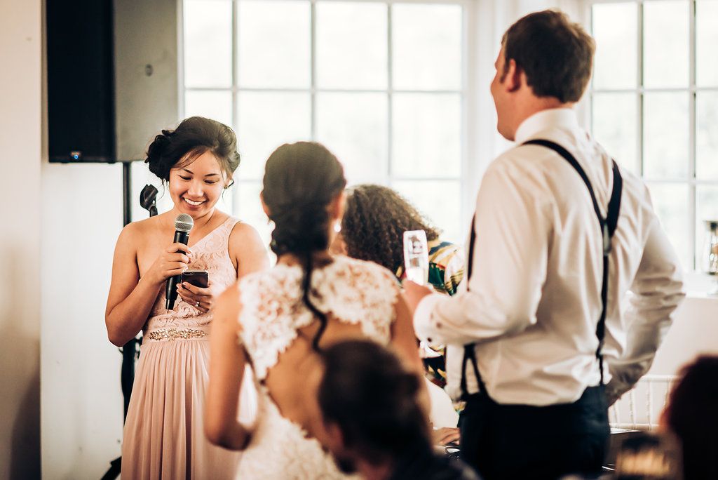 A speech being delivered at an elegant wedding reception while guests listen attentively in a bright venue.