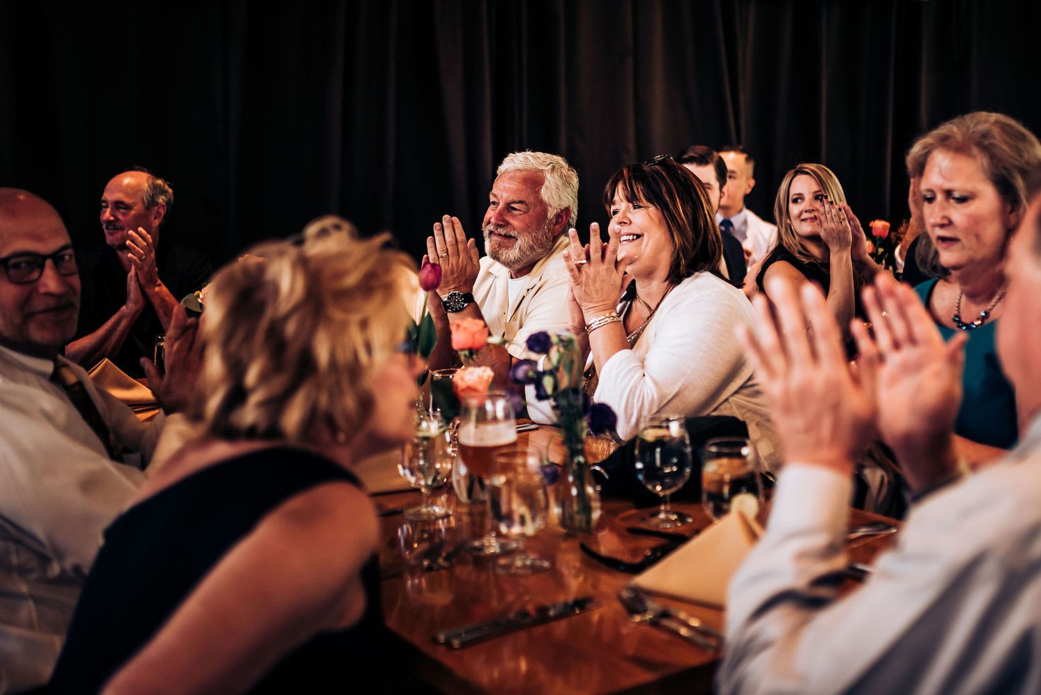 Guests celebrating and raising hands at a dimly lit reception dinner.