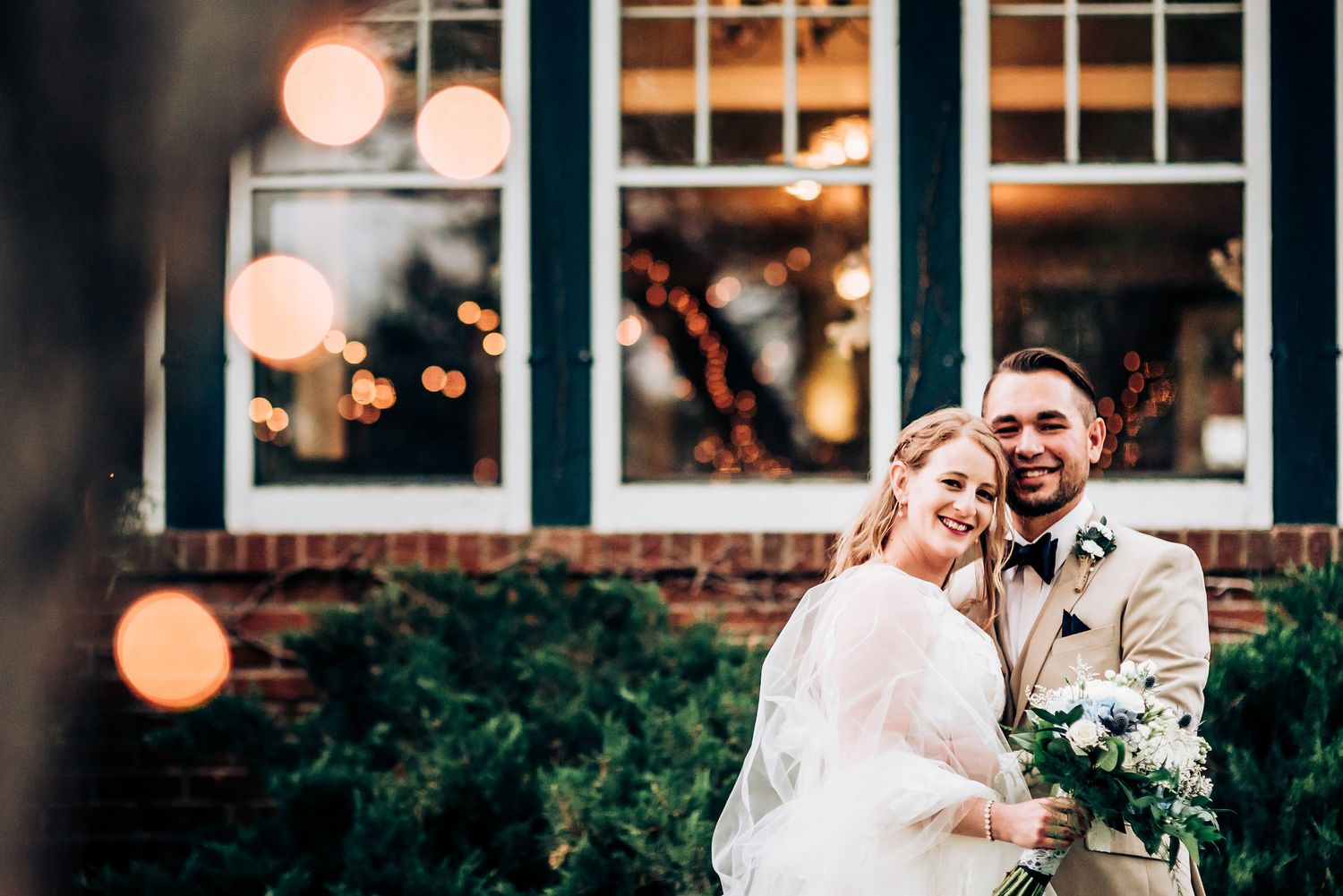 A wedding celebration outside a brick building with twinkling lights creating a magical evening atmosphere.