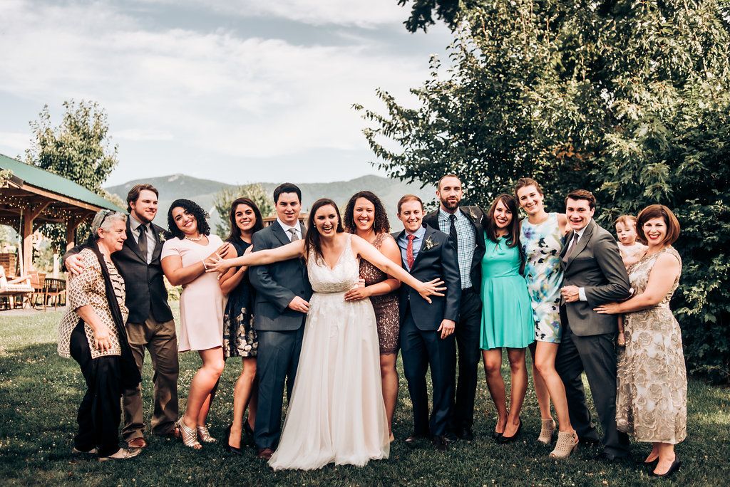 Group photo of wedding party and guests posing together at outdoor venue.
