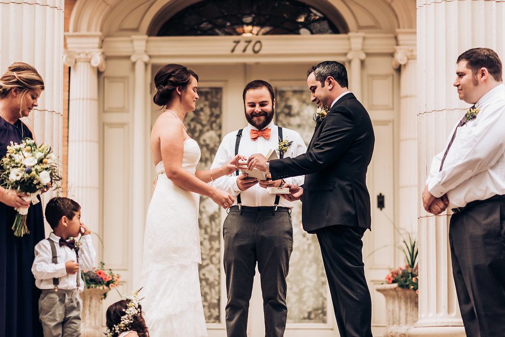 A wedding ceremony underway on ornate building steps with white columns and an arched doorway.