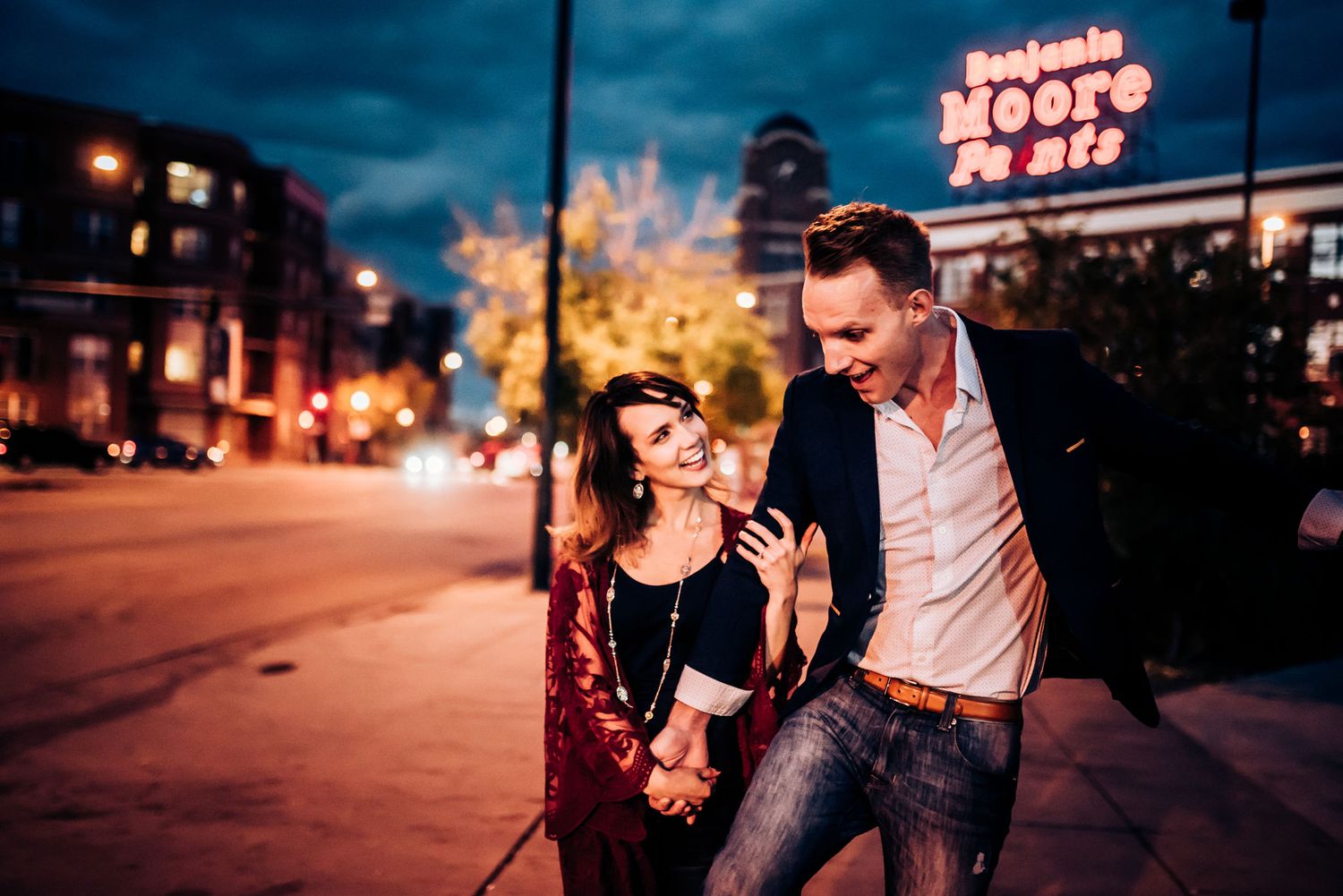 A couple shares a playful moment on an urban street at night.