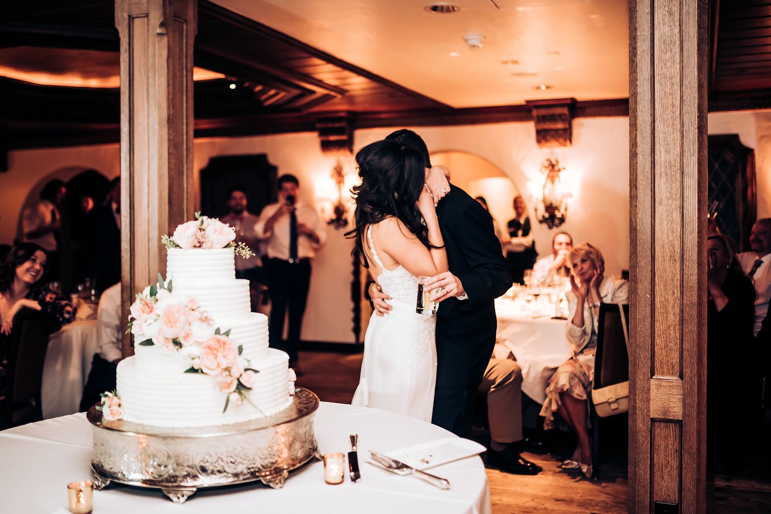 Romantic celebration moment beside an elegant tiered wedding cake decorated with flowers.