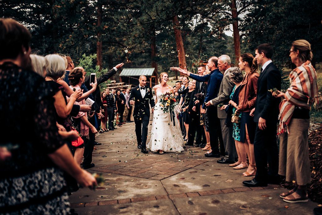 Wedding guests form aisle for newlyweds exit while throwing celebratory items outdoors.