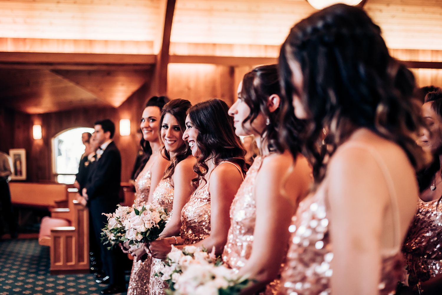 Bridesmaids in matching pink dresses stand in a row holding bouquets during wedding ceremony.