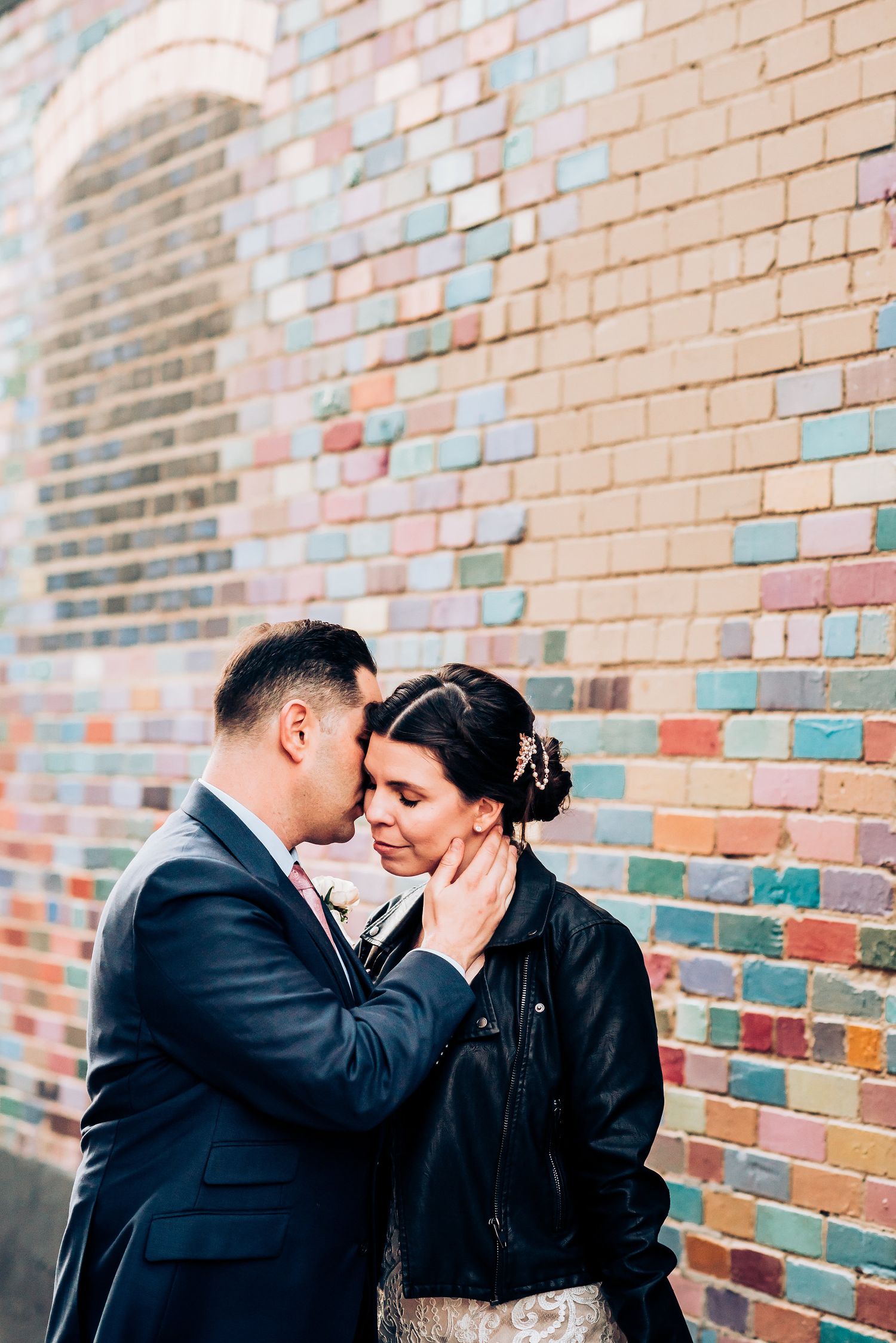 Intimate wedding portrait against pastel colored brick wall background.