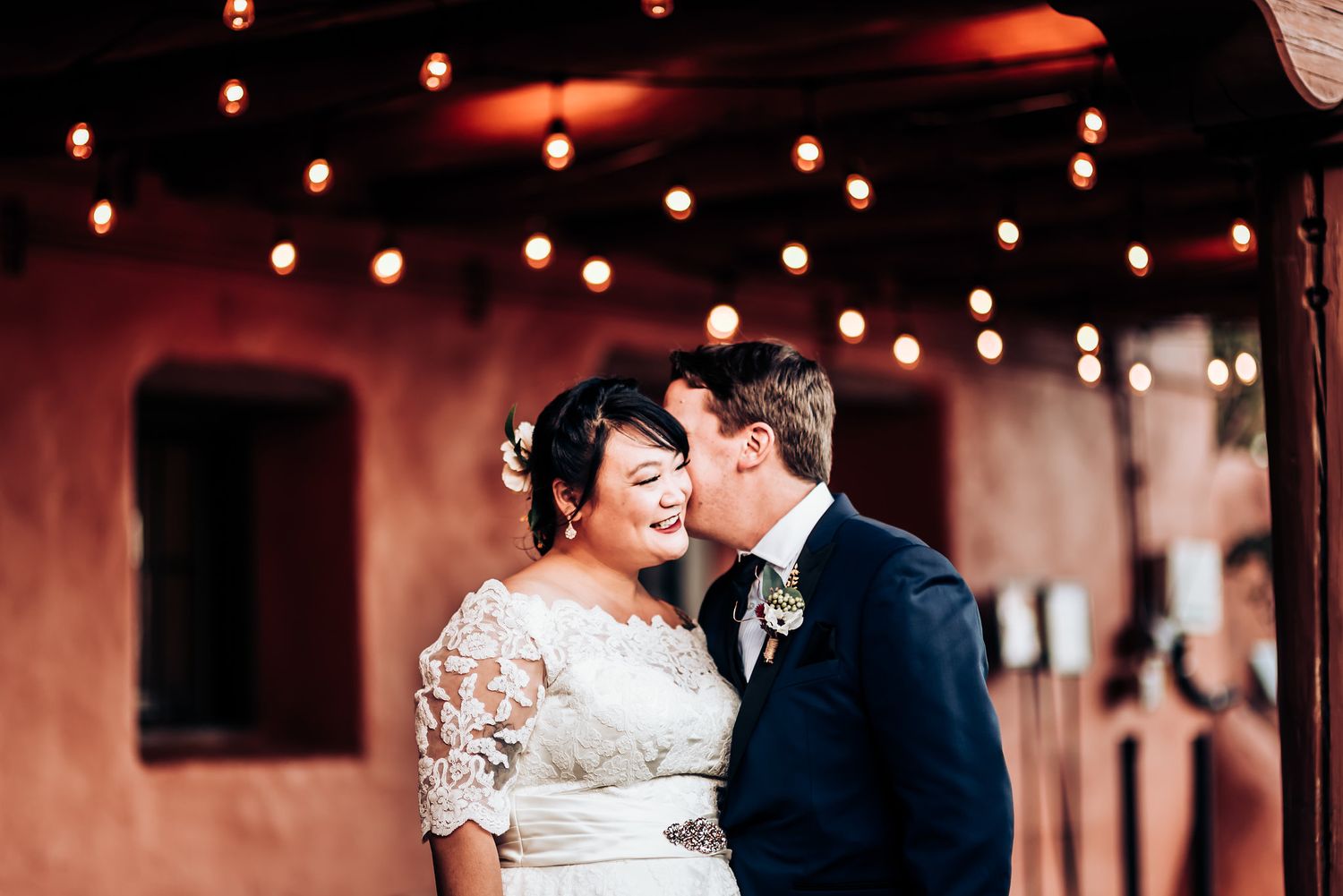 Romantic moment captured under glowing string lights at outdoor venue.