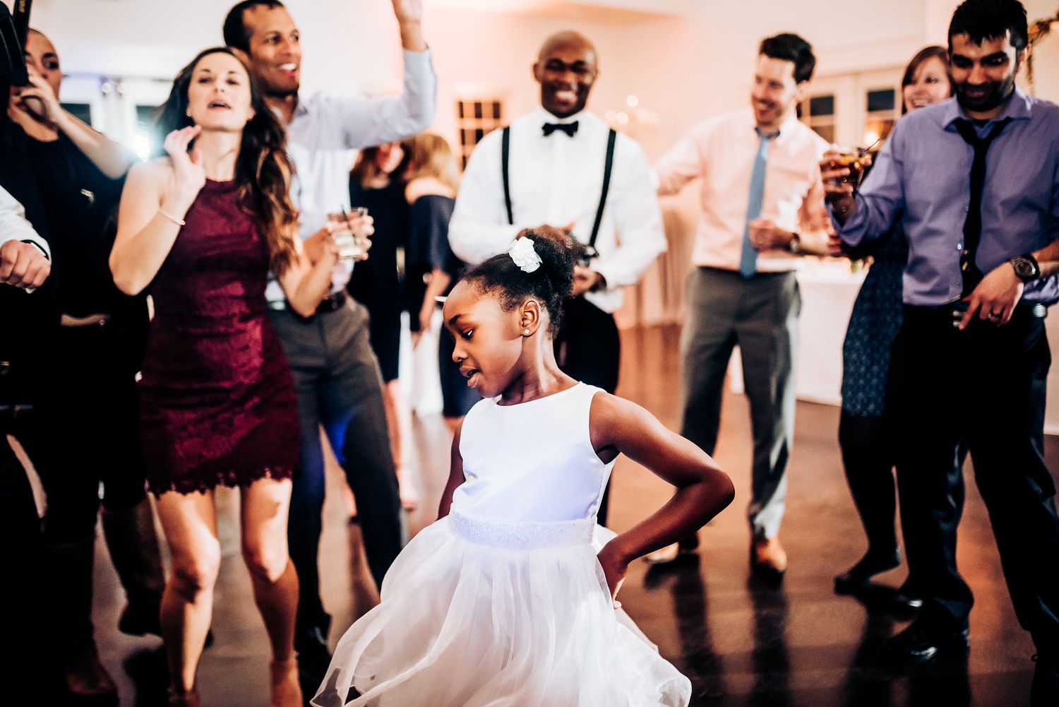 Young guest shows off dance moves while others watch at wedding reception.