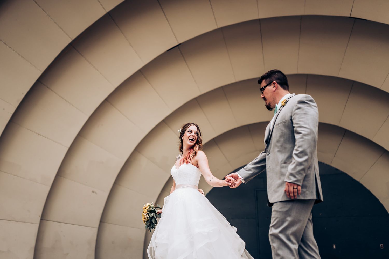 A wedding photograph taken against a curved architectural background with concentric circles.