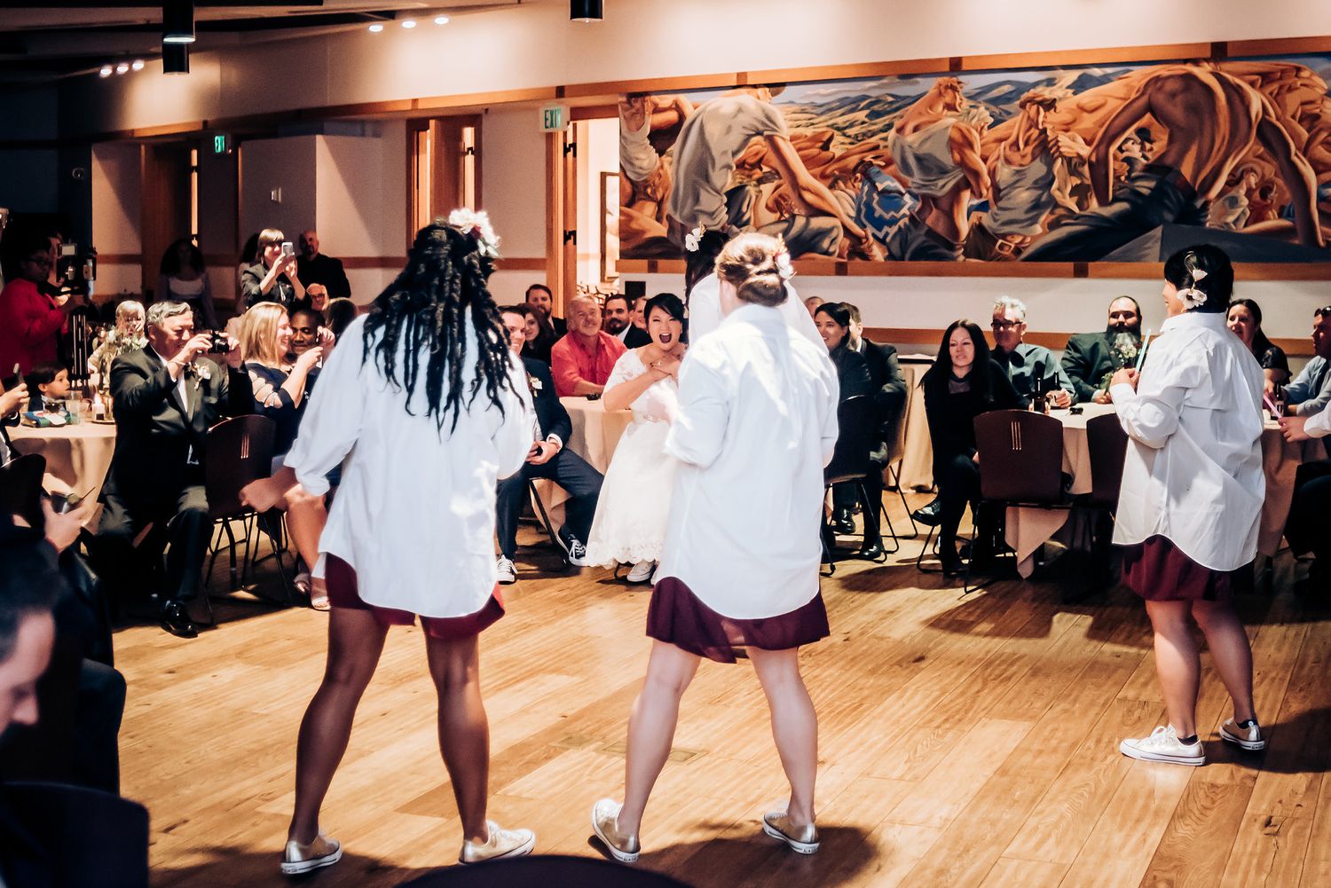 Dancers in white shirts and casual attire perform energetic moves on a wooden dance floor.