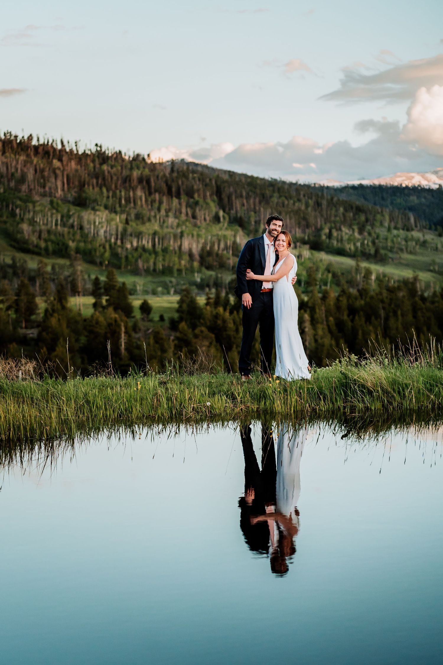 Elegant wedding portrait by mountain lake showing perfect reflection in still waters.