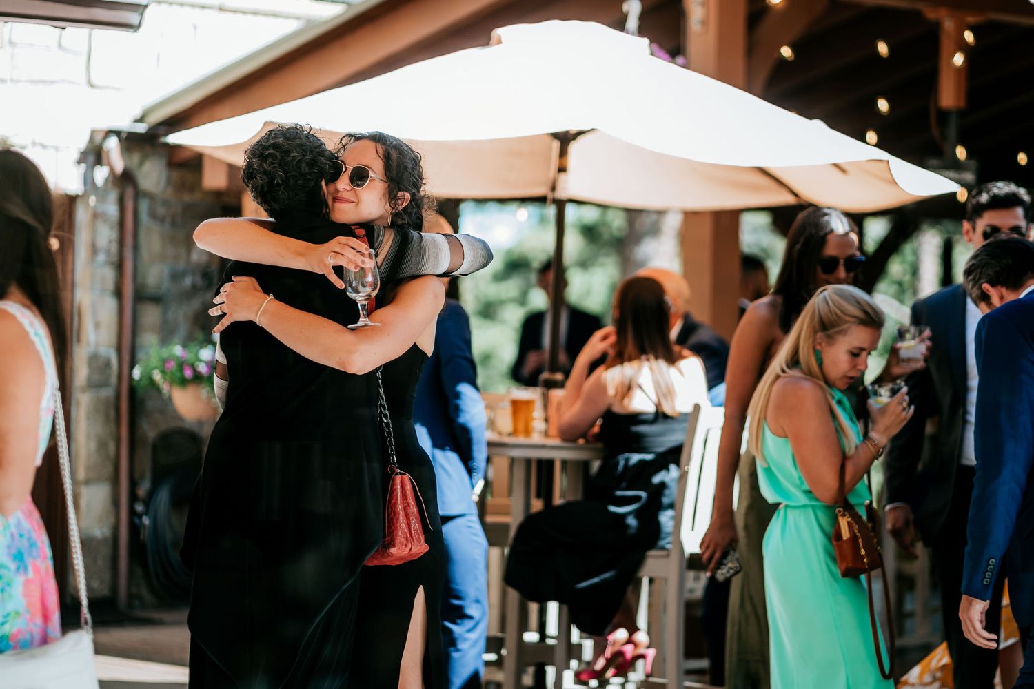 Wedding guests dancing and embracing under white umbrellas at an outdoor reception.