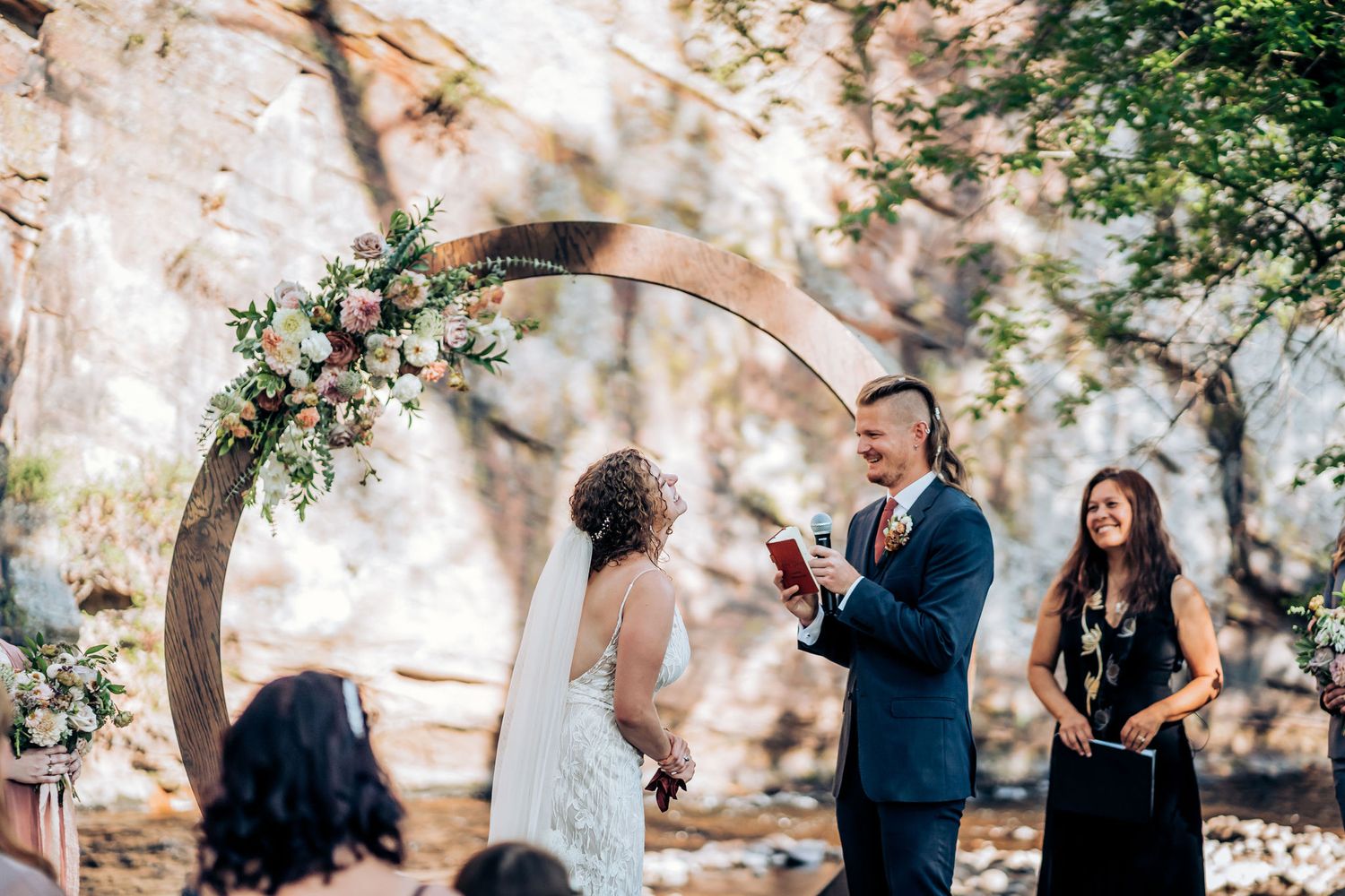 Wedding ceremony taking place beneath a decorated circular arch with floral arrangements.