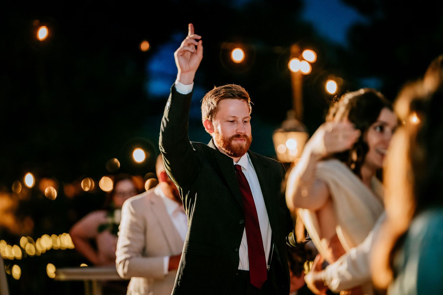 Wedding guest dancing with raised arm under string lights at outdoor reception.